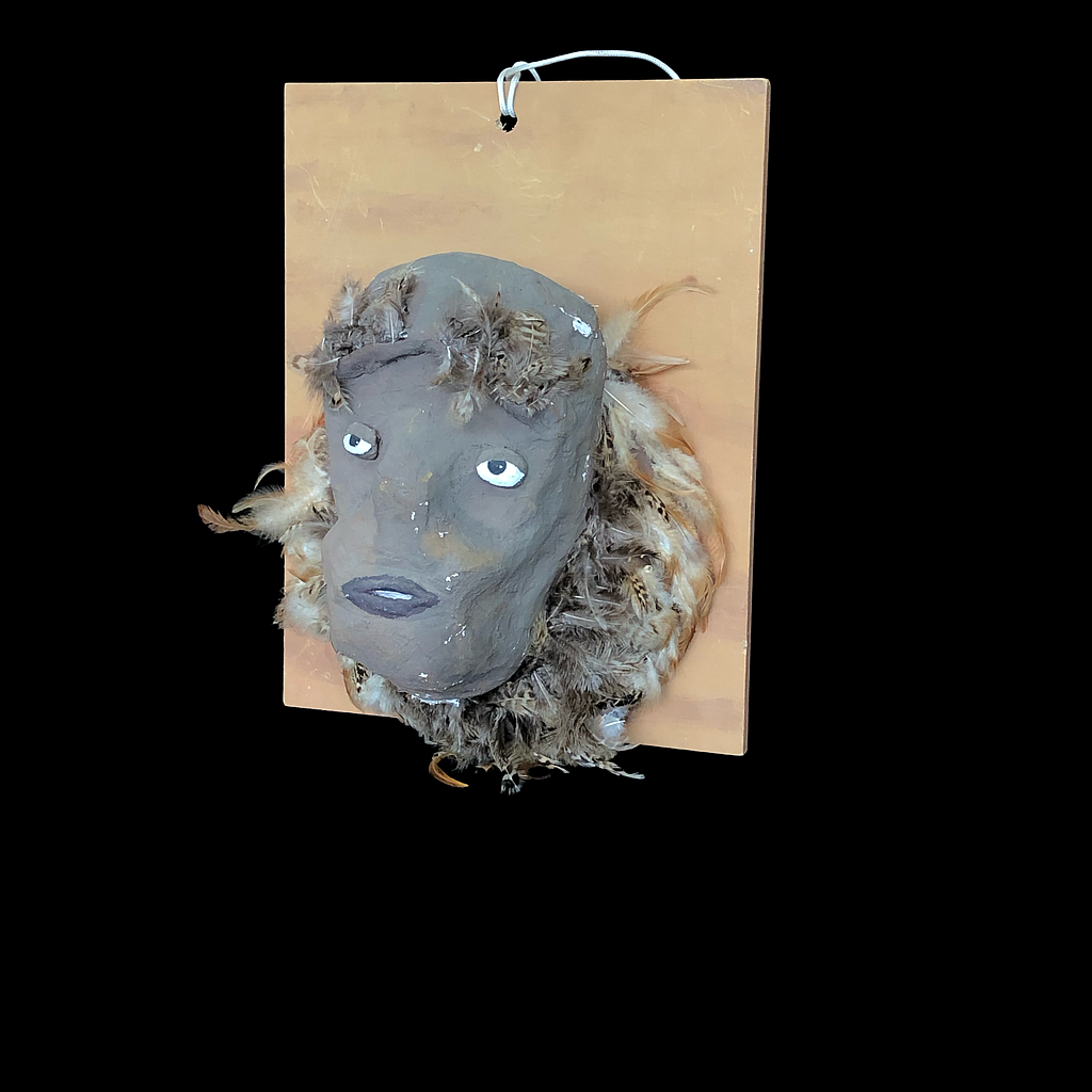 graue Maske aus Pappmaché mit Federschmuck auf Holzbrett